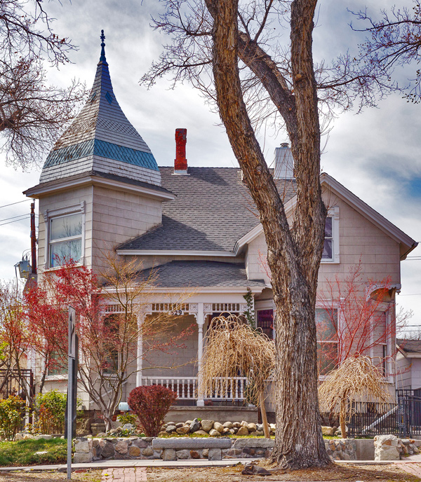 The 829 Center Street home is white with blue trim. A decorated front porch has cute, early twentieth century railings. a turret rises above the home.